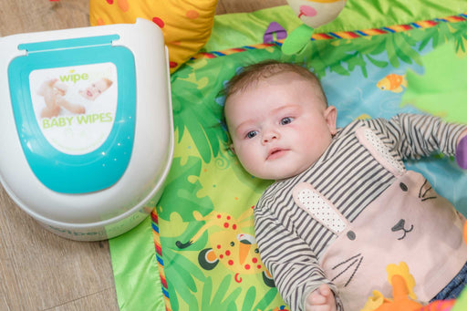 Wipepod® Dispenser with baby on colorful play mat, featuring ultra-soft baby wipes for easy changes.