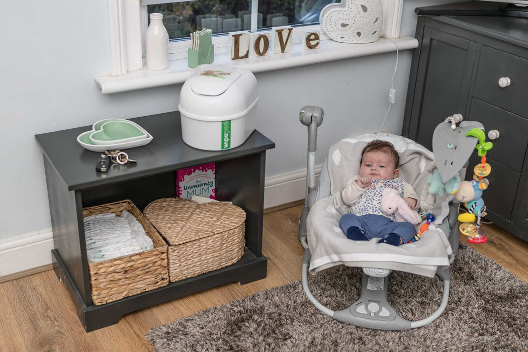 Wipepod® Dispenser with ultra-soft baby wipes on nursery shelf next to baby in rocker.